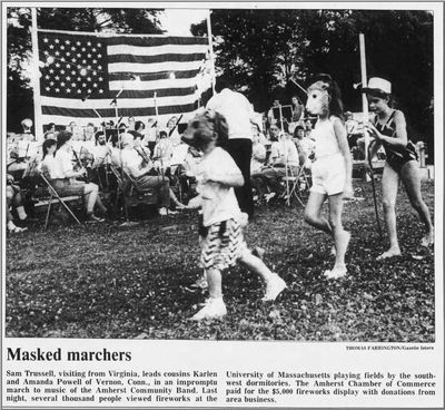 Daily Hampshire Gazette feature from July 5, 1990 about the Amherst Community Band playing during fireworks. Caption reads: Masked marches: Sam Trussell, visiting from Virginia, leads cousins Karlen and Amanda Powell of Veron, Conn., in an impromptu march to the music of the Amherst Community Band. Last night, several thousand people viewed fireworks at the University of Massachusetts playing fields by the south-west dormitories. The Amherst Chamber of Commerce paid for the $5,000 fireworks display with donations from area business.